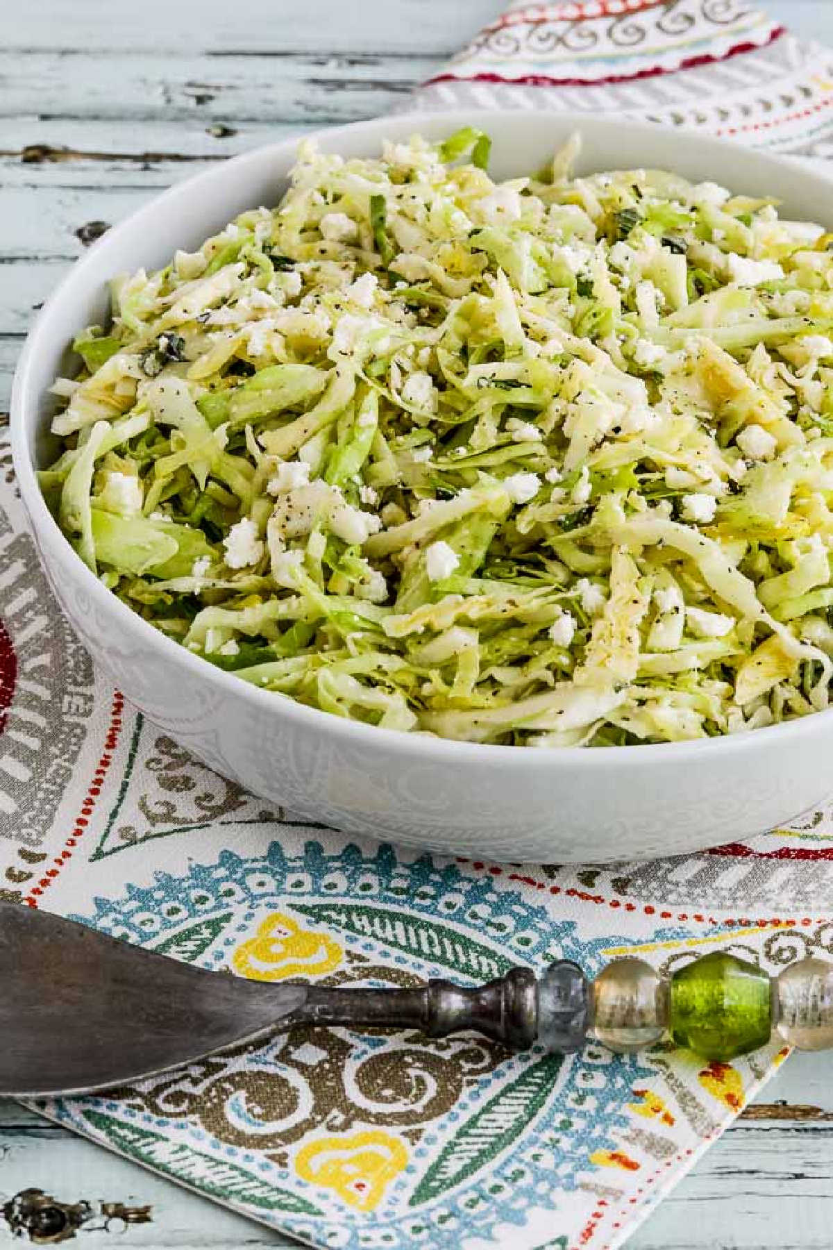 Greek Cabbage Salad in serving bowl with green serving fork and napkin