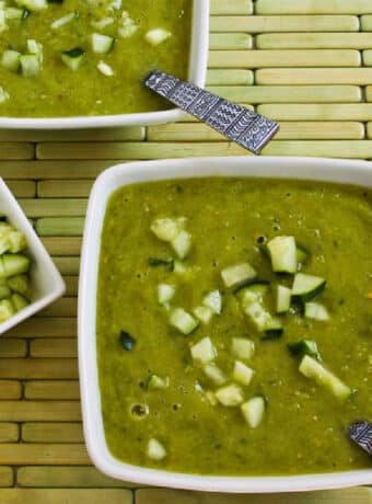Green Gazpacho in two serving bowls with chopped cucumbers for garnish