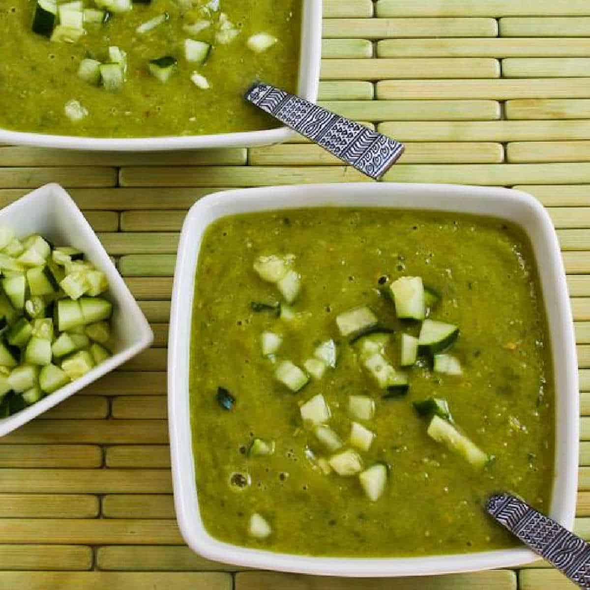 Green Gazpacho in two serving bowls with chopped cucumbers for garnish