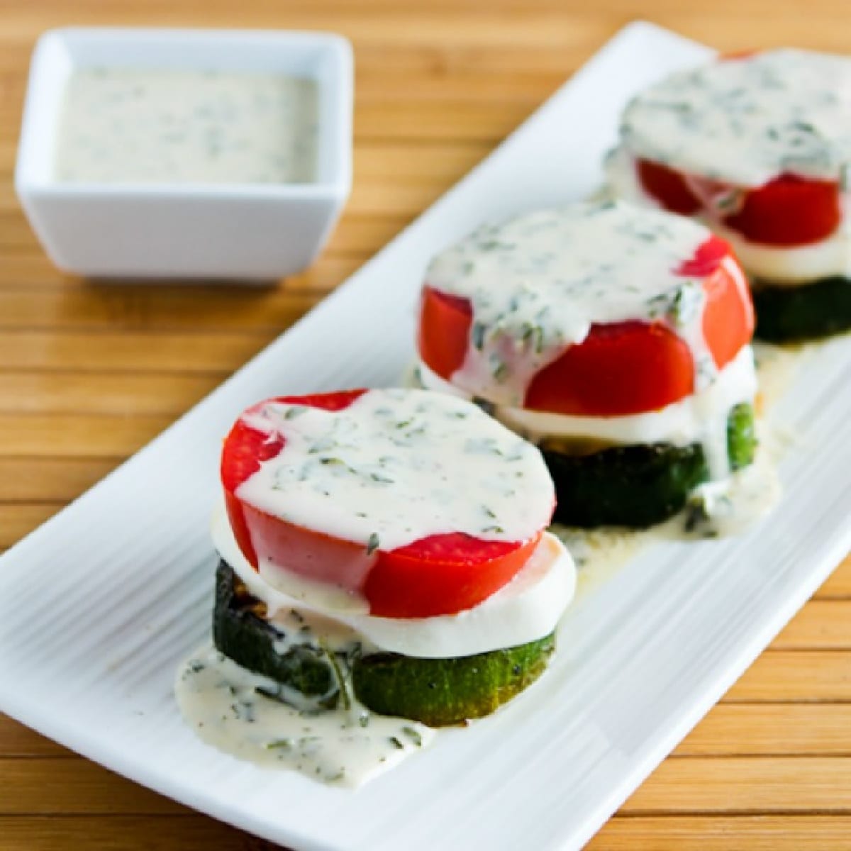 Square image of grilled zucchini caprese salad on a serving plate.