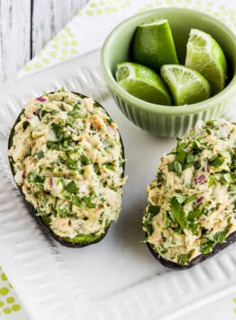 Tuna Stuffed Avocado shown with two avocado halves on serving plate with cut limes