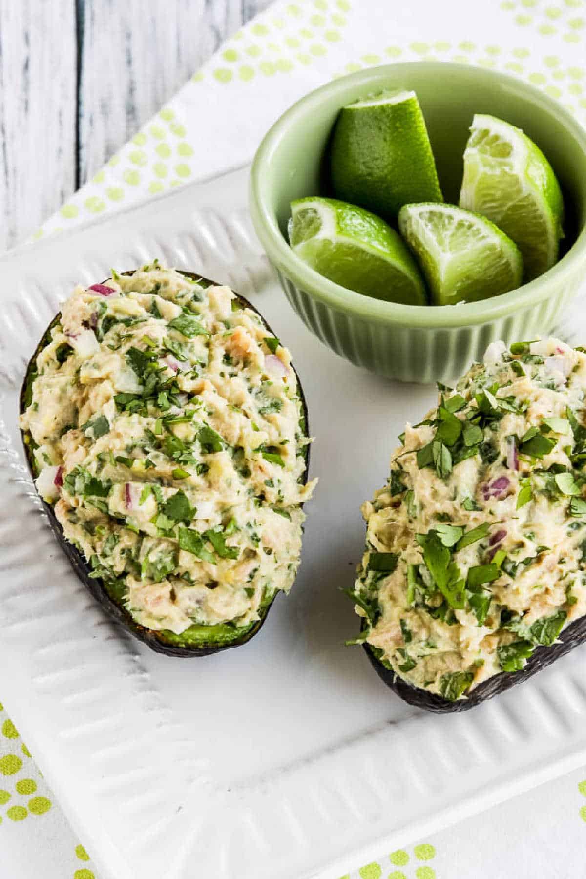 Tuna Stuffed Avocado shown with two avocado halves on serving plate with cut limes