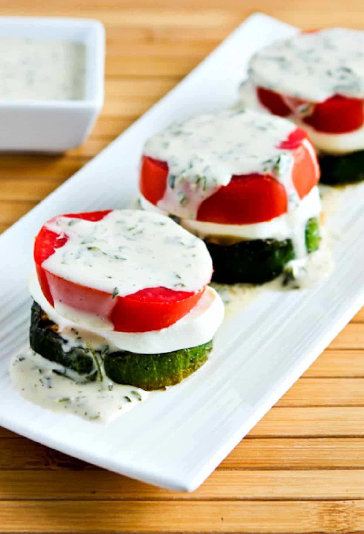 Layered grilled zucchini caprese on platter served with basil vinaigrette