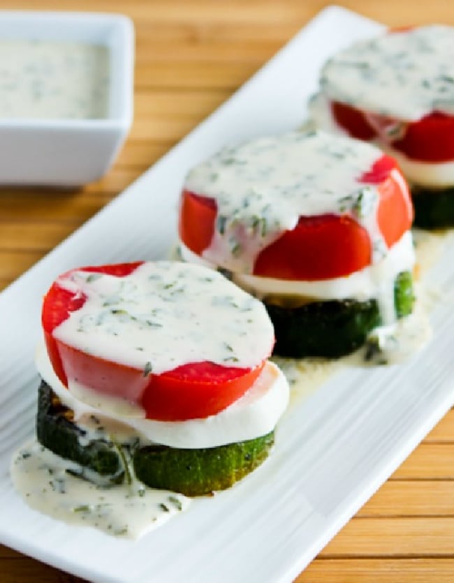 Grilled zucchini caprese stacks on serving plate with basil sauce dressing in background, close-up