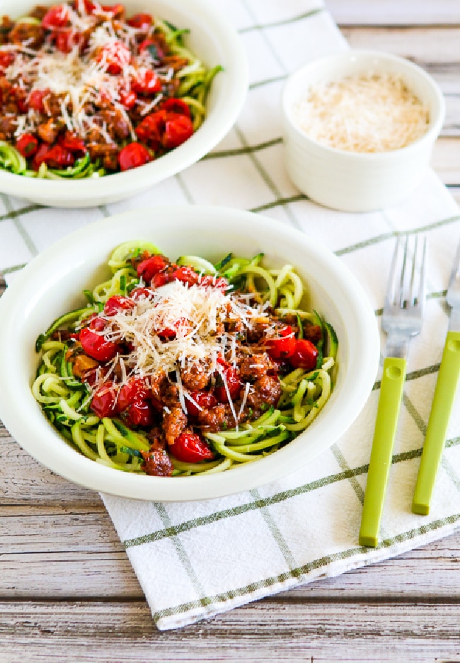 Zucchini noodles with cherry tomato pasta sauce in two serving bowls with parmesan cheese on the side.