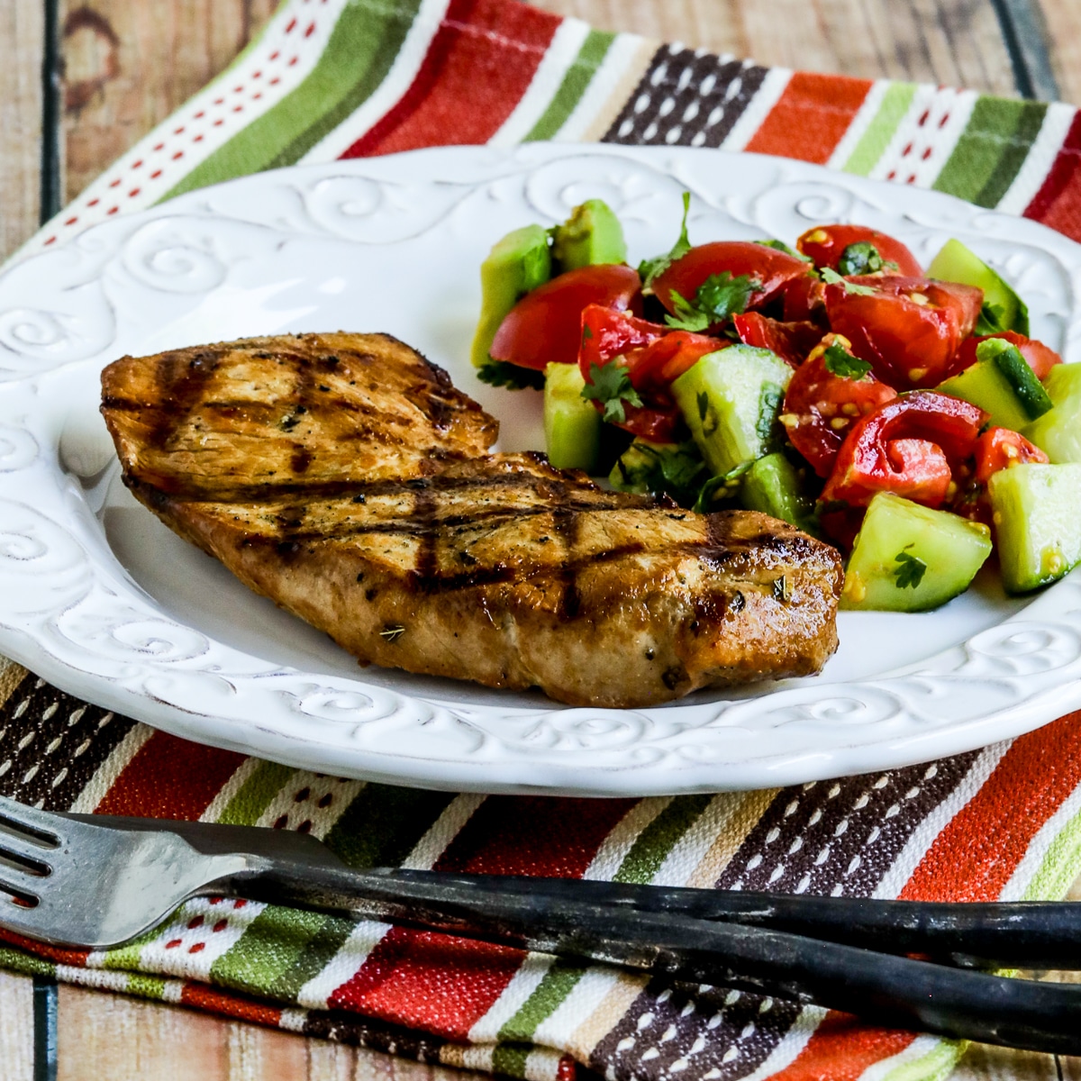 Square image of Marinated Grilled Pork Sirloin Chops shown on plate with fork and knife.