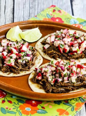 Square image of Spicy Shredded Beef Street Tacos with three open tacos on serving platter topped with radish salsa.