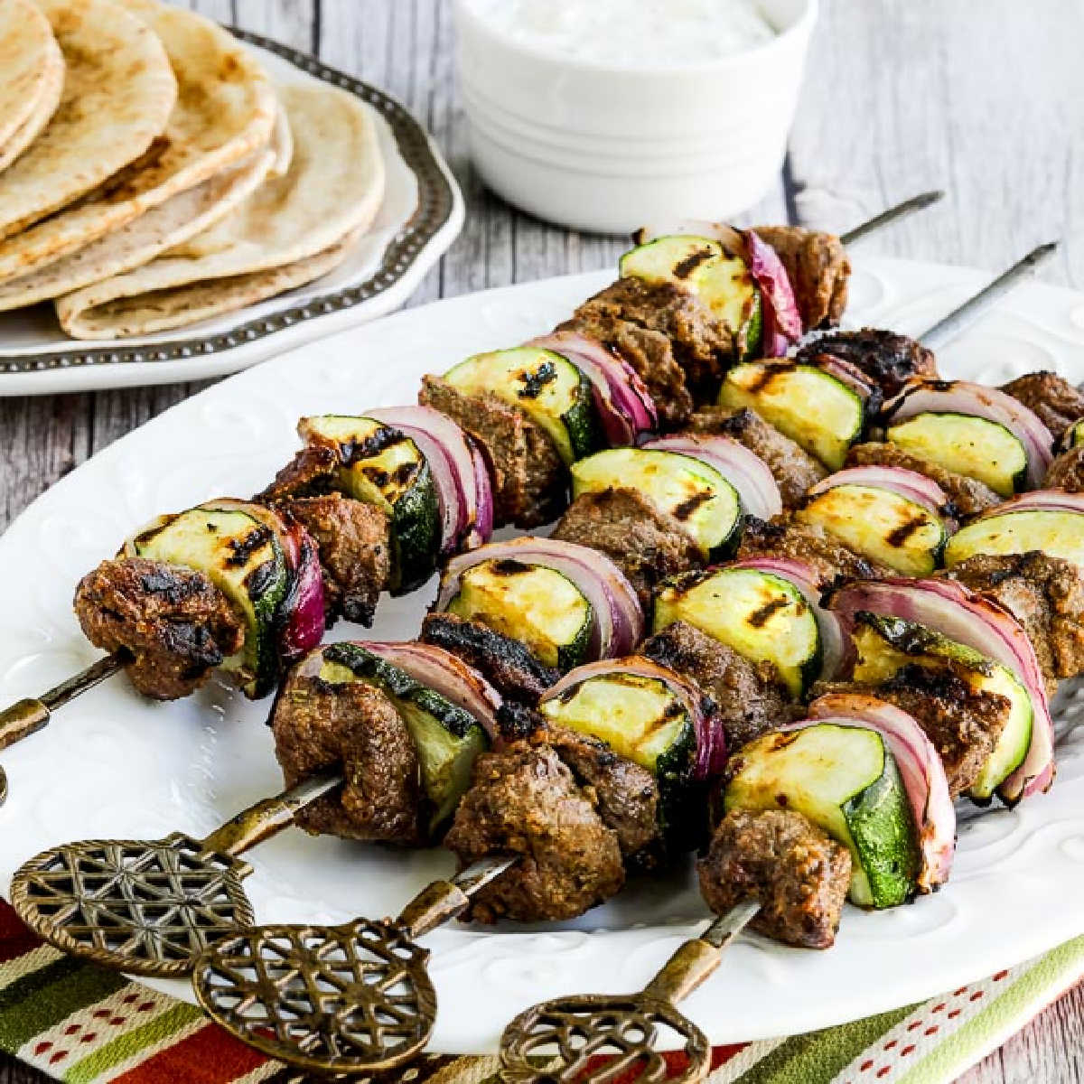 Low-Carb Lamb Shish Kabobs shown on serving plate with low-carb pita in back