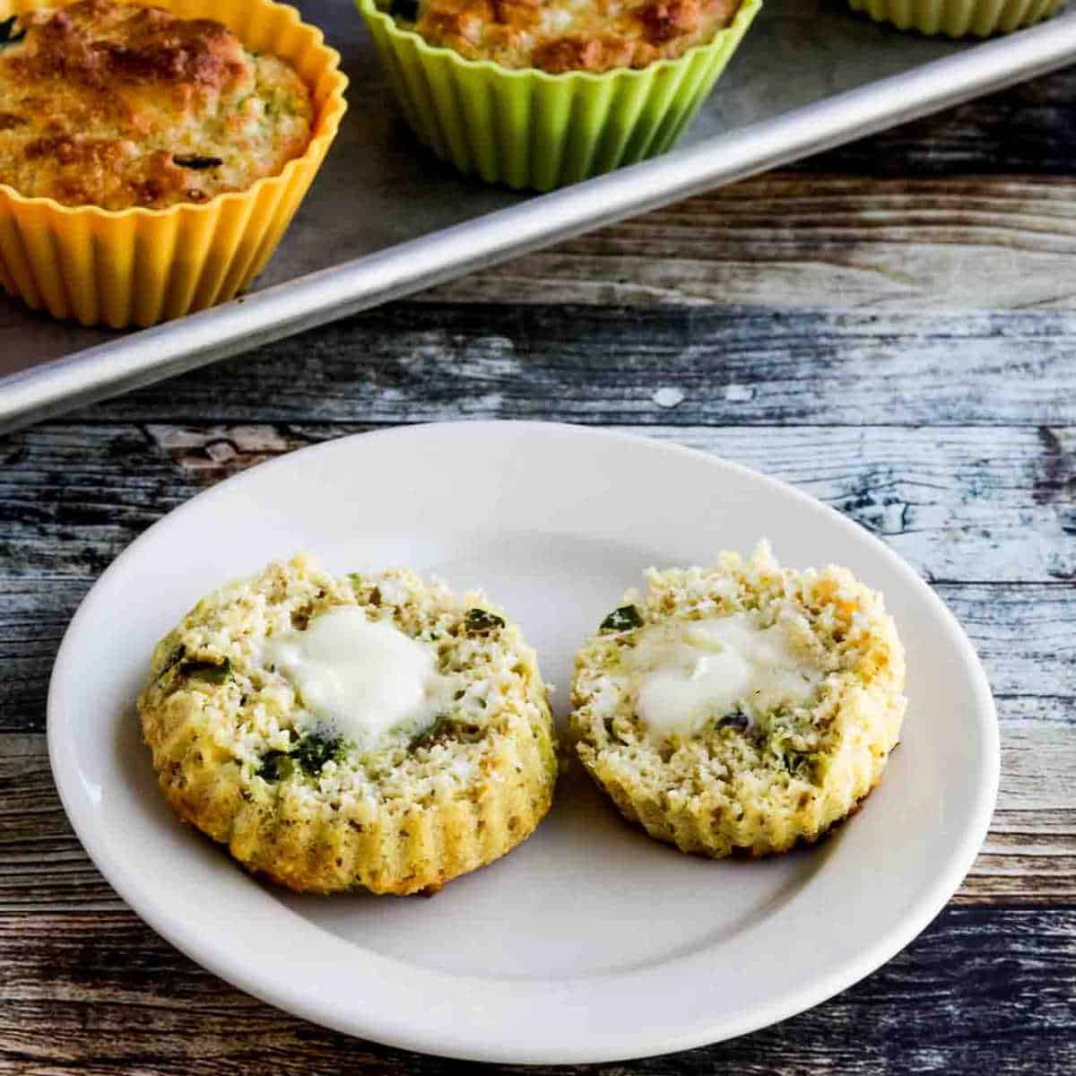 Flourless Breakfast Muffins with Zucchini and Feta shown on serving plate with muffin cut in half with butter