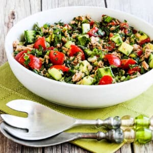 Tuna Salad with Cucumbers, Tomatoes, Parsley, and Mint shown in serving bowl on green napkin with green serving forks.