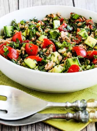 Tuna Salad with Cucumbers, Tomatoes, Parsley, and Mint shown in serving bowl on green napkin with green serving forks.