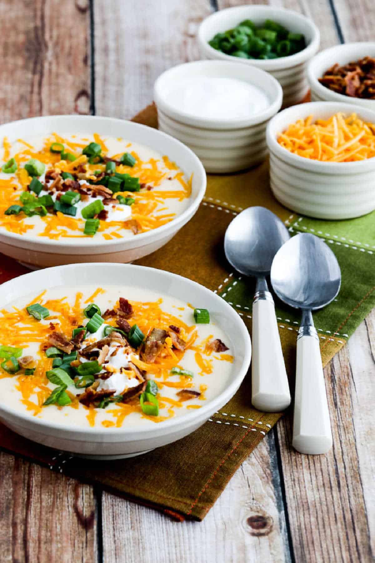 Instant Pot Loaded Cauliflower Soup with soup in two bowls, spoons, and toppings in background