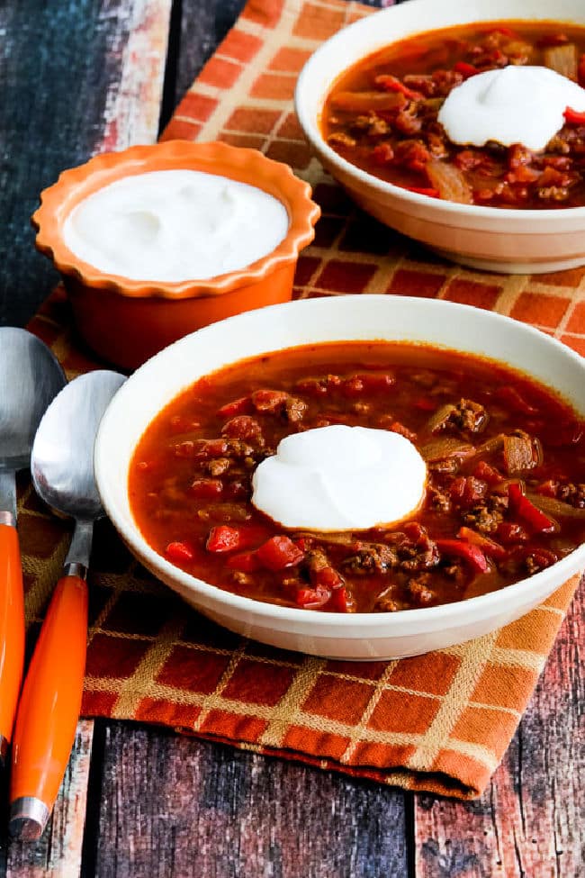 Instant Pot Goulash Soup in two serving bowls with sour cream and orange spoons.