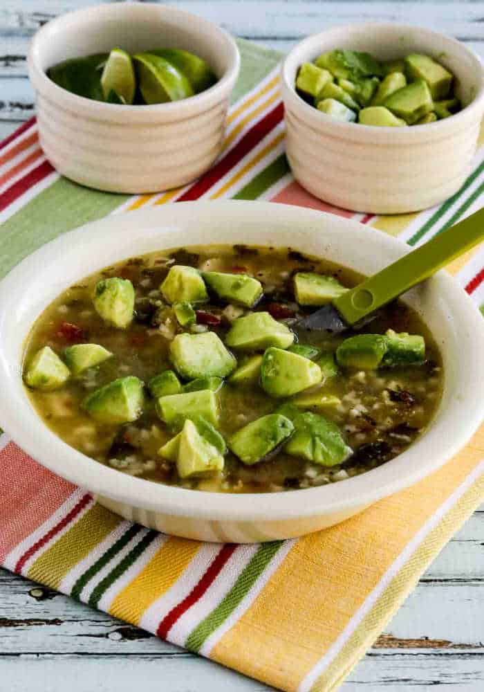 Chicken Tomatillo Soup shown in serving bowl with limes and avocados on the side