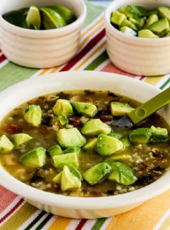 Chicken Tomatillo Soup in bowl with limes and avocado in back