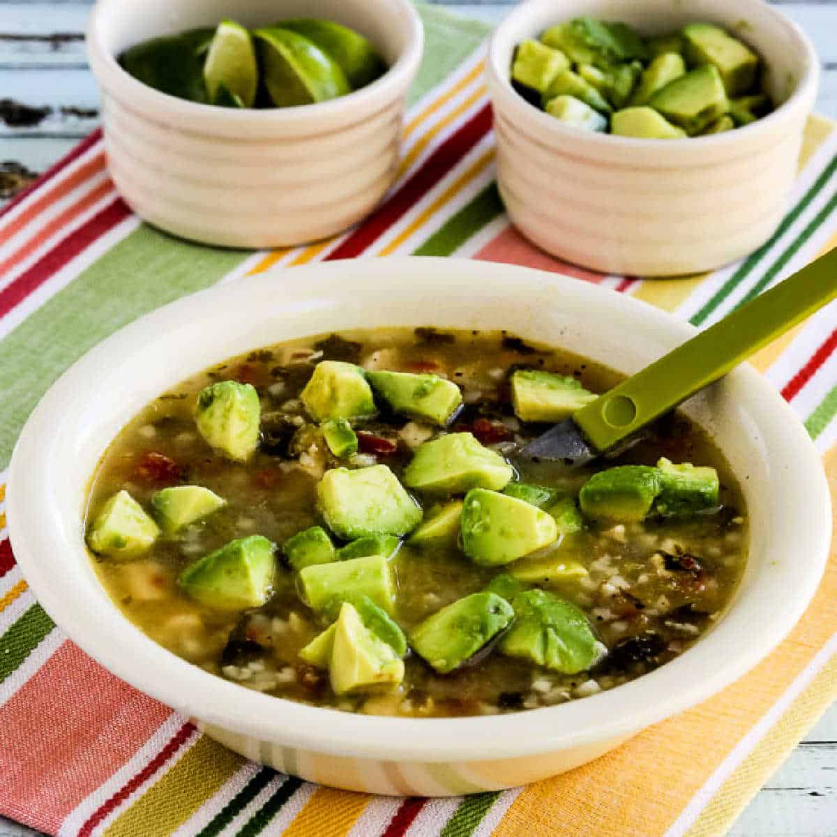Chicken Tomatillo Soup in bowl with limes and avocado in back