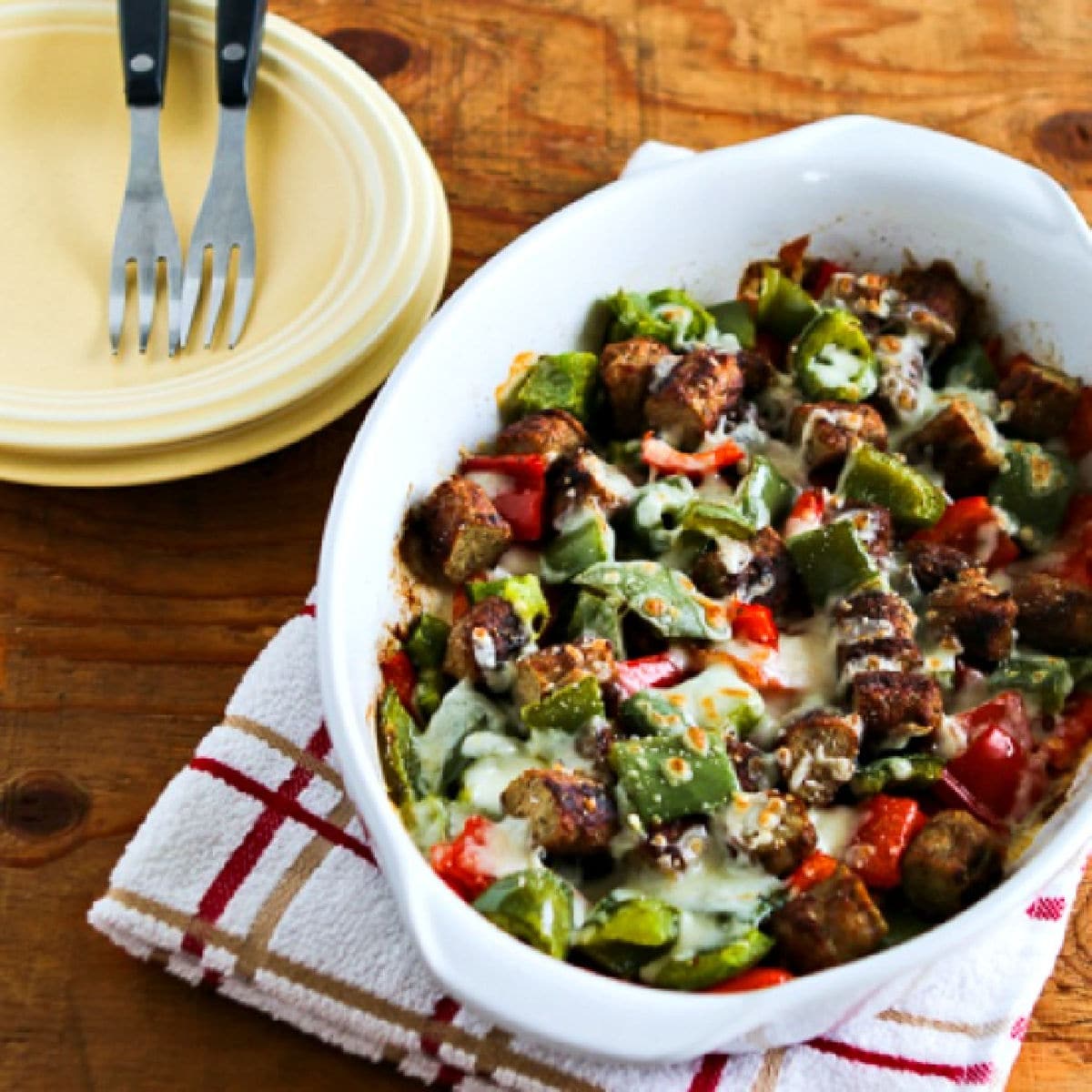 Square image of Low-Carb No-Egg Breakfast Bake with Sausage and Peppers in baking dish with plates, forks.