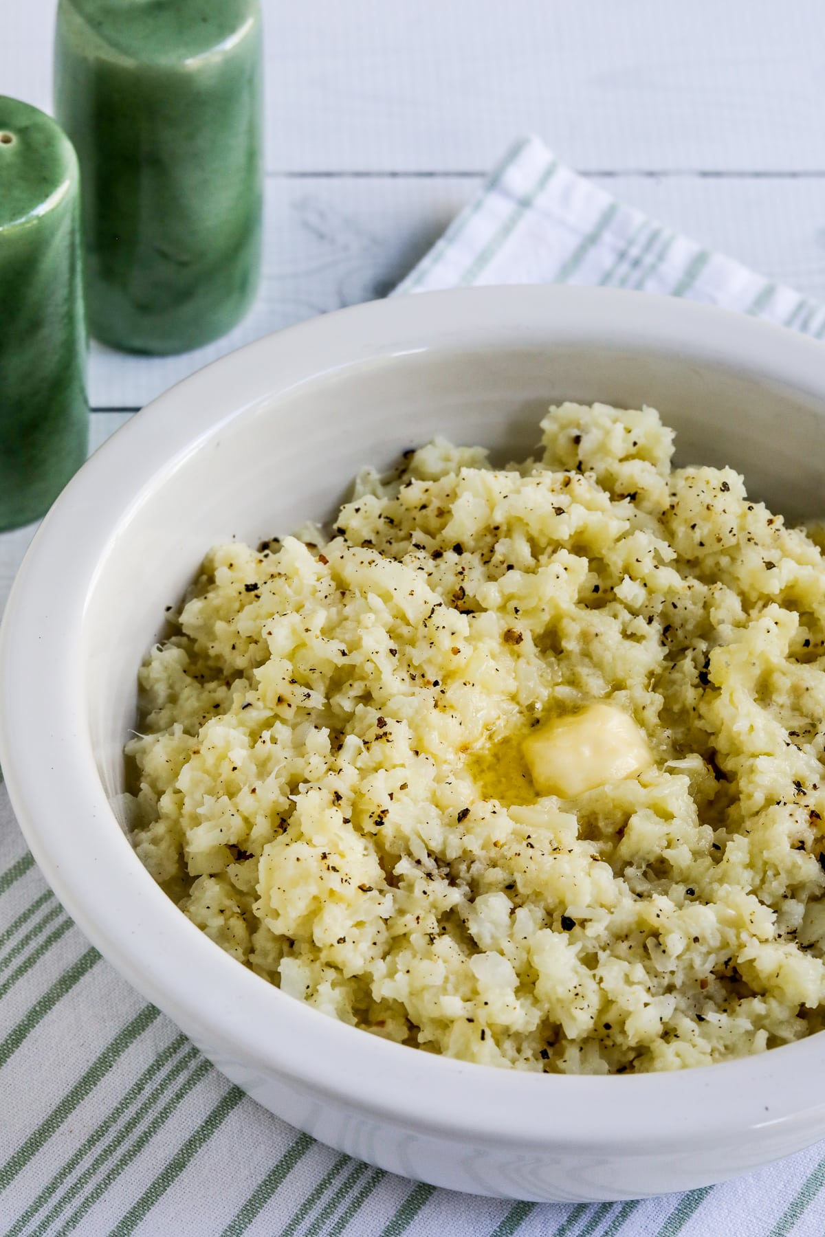 Pureed Cauliflower with Garlic, Parmesan, and Goat Cheese shown in bowl with spoon and salt-pepper shakers.