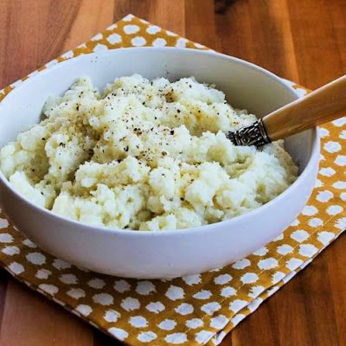 Square image for Pureed Cauliflower with Garlic, Parmesan, and Goat Cheese shown in serving bowl with spoon.