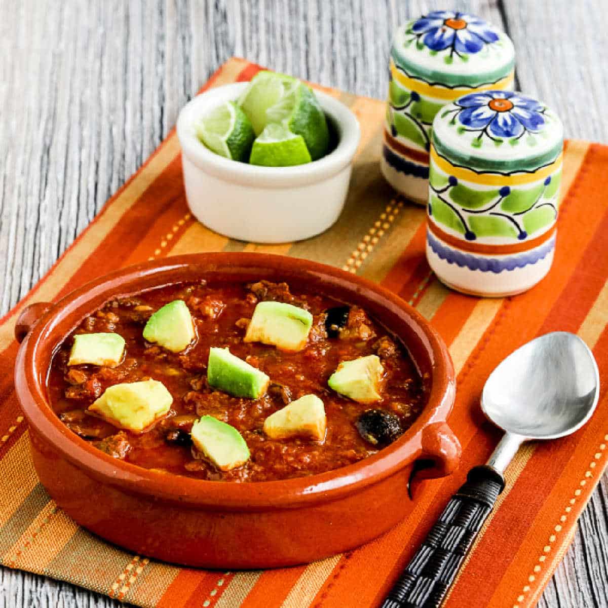 Square image for Low-Carb Southwestern Beef Stew shown in terra cotta bowl with limes and Mexican salt and pepper shakers.
