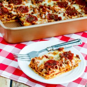 Square image of Sausage and Pepperoni Layered Pizza Bake in baking pan with one piece on plate.