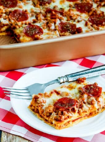 Square image of Sausage and Pepperoni Layered Pizza Bake in baking pan with one piece on plate.