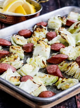 square image of Cabbage and Sausage Sheet Pan Meal on baking sheet with lemons in background