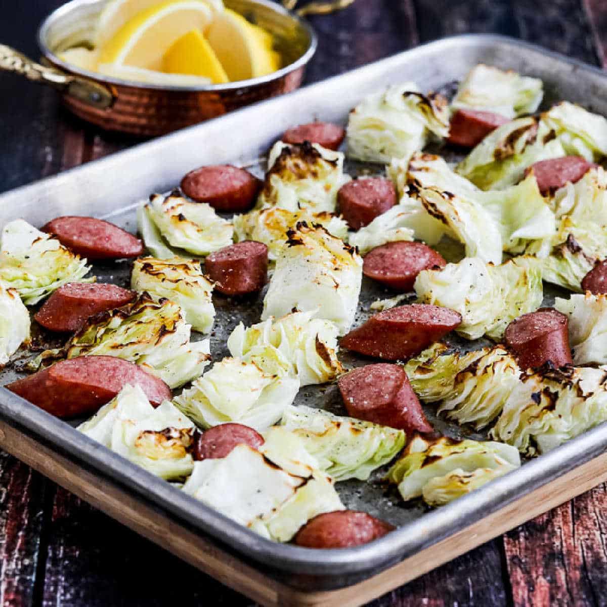 square image of Cabbage and Sausage Sheet Pan Meal on baking sheet with lemons in background