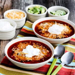 Square image of Instant Pot Taco Soup shown in two serving bowls with sour cream, cheese, limes, and avocado in background.