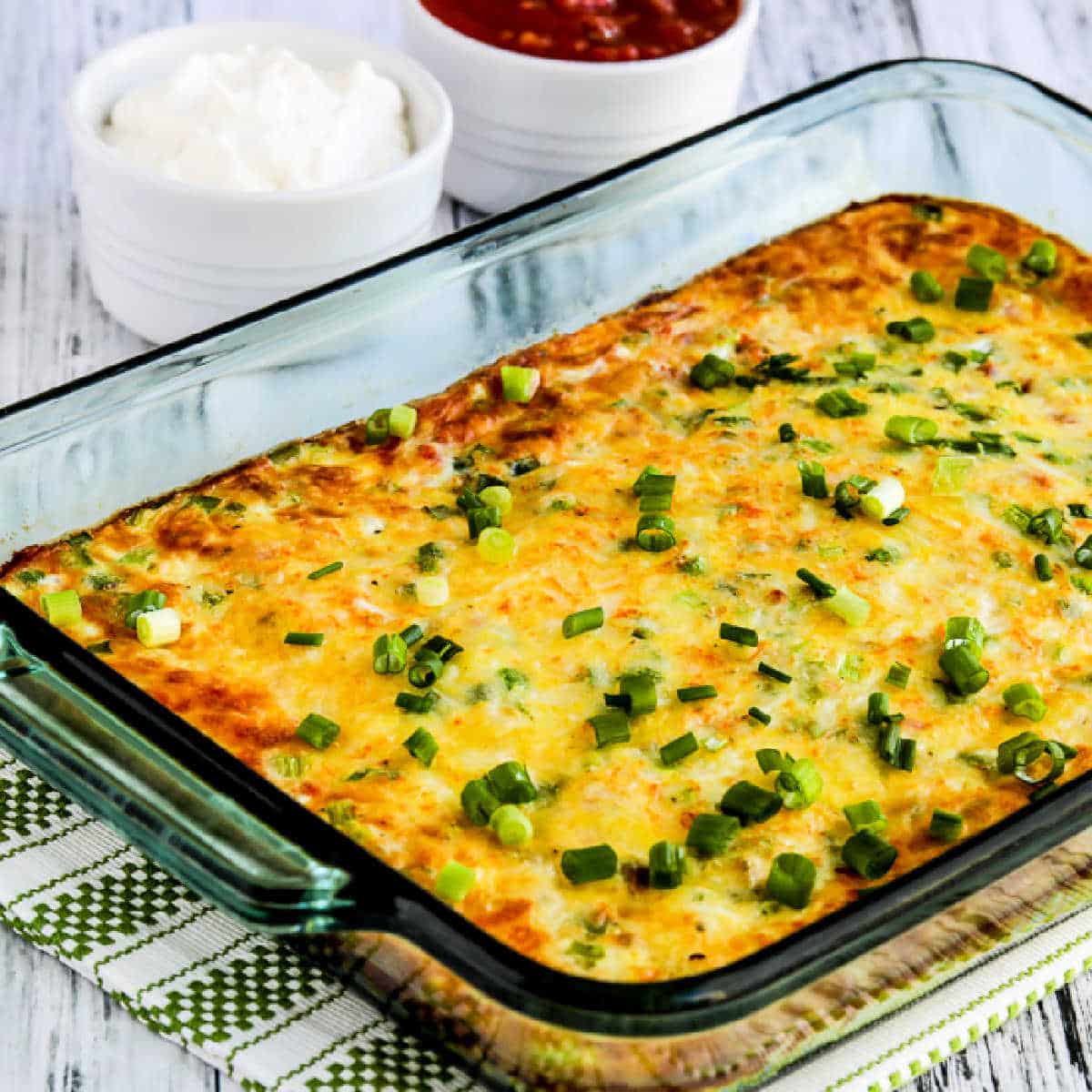 Square image for Southwest Egg Casserole in baking dish with salsa and sour cream in the background.