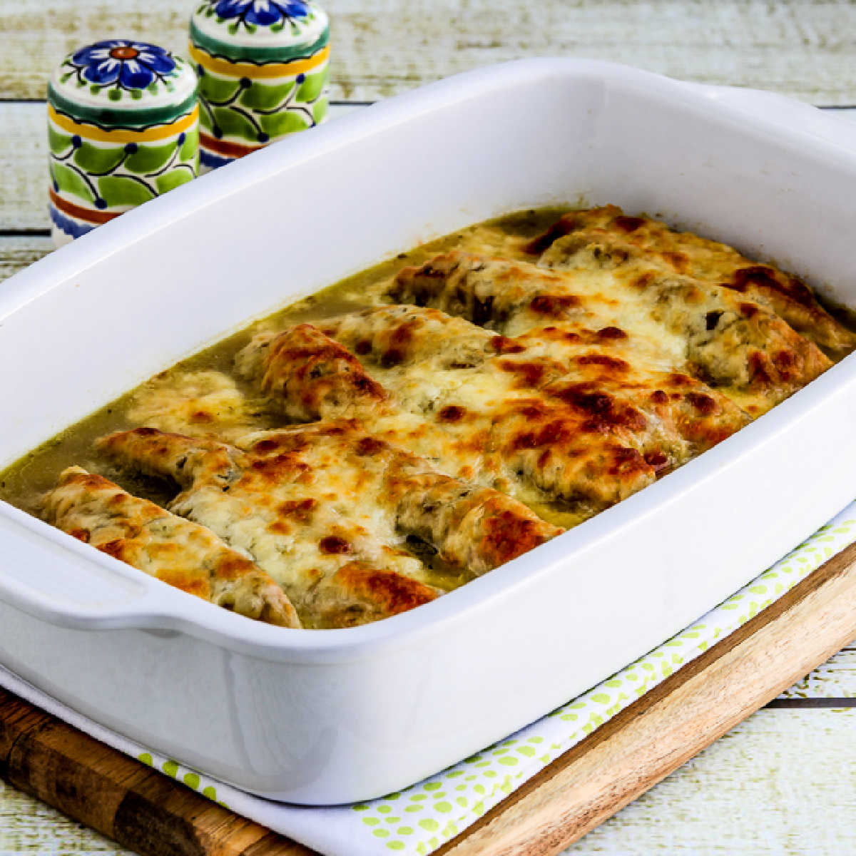 Square image of Salsa Verde Chicken Bake shown in baking dish with Mexican salt-pepper shakers in background.