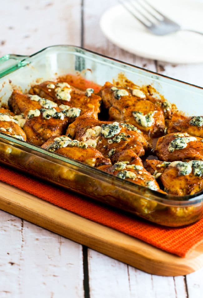Baked Buffalo Chicken with Melted Blue Cheese shown in baking dish on cutting board.