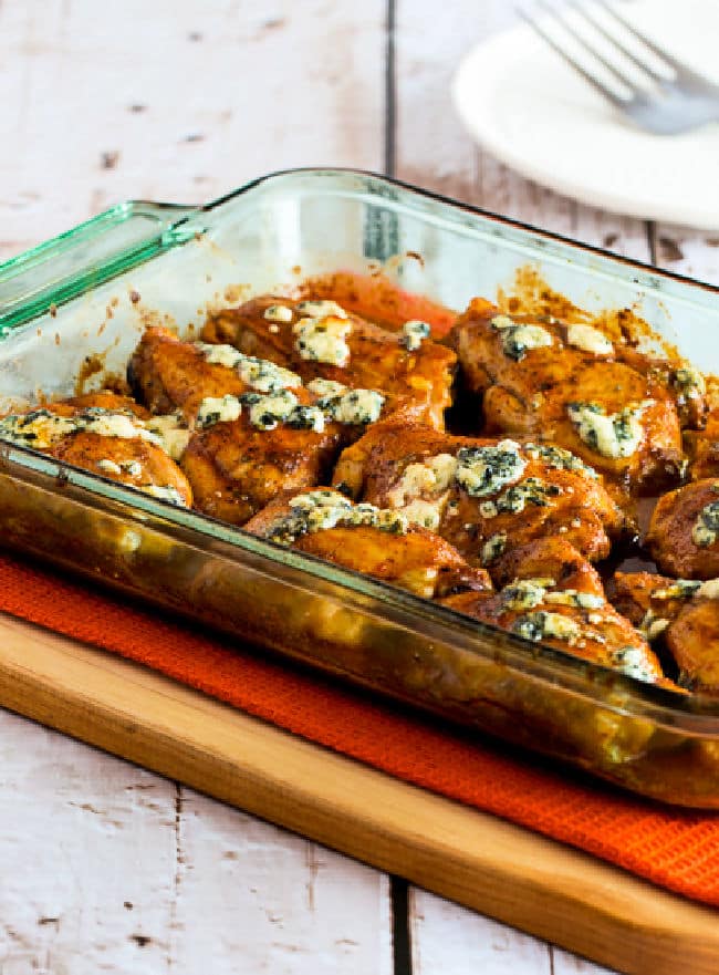 Cropped image of Baked Buffalo Chicken with Melted Blue Cheese shown in baking dish on cutting board.