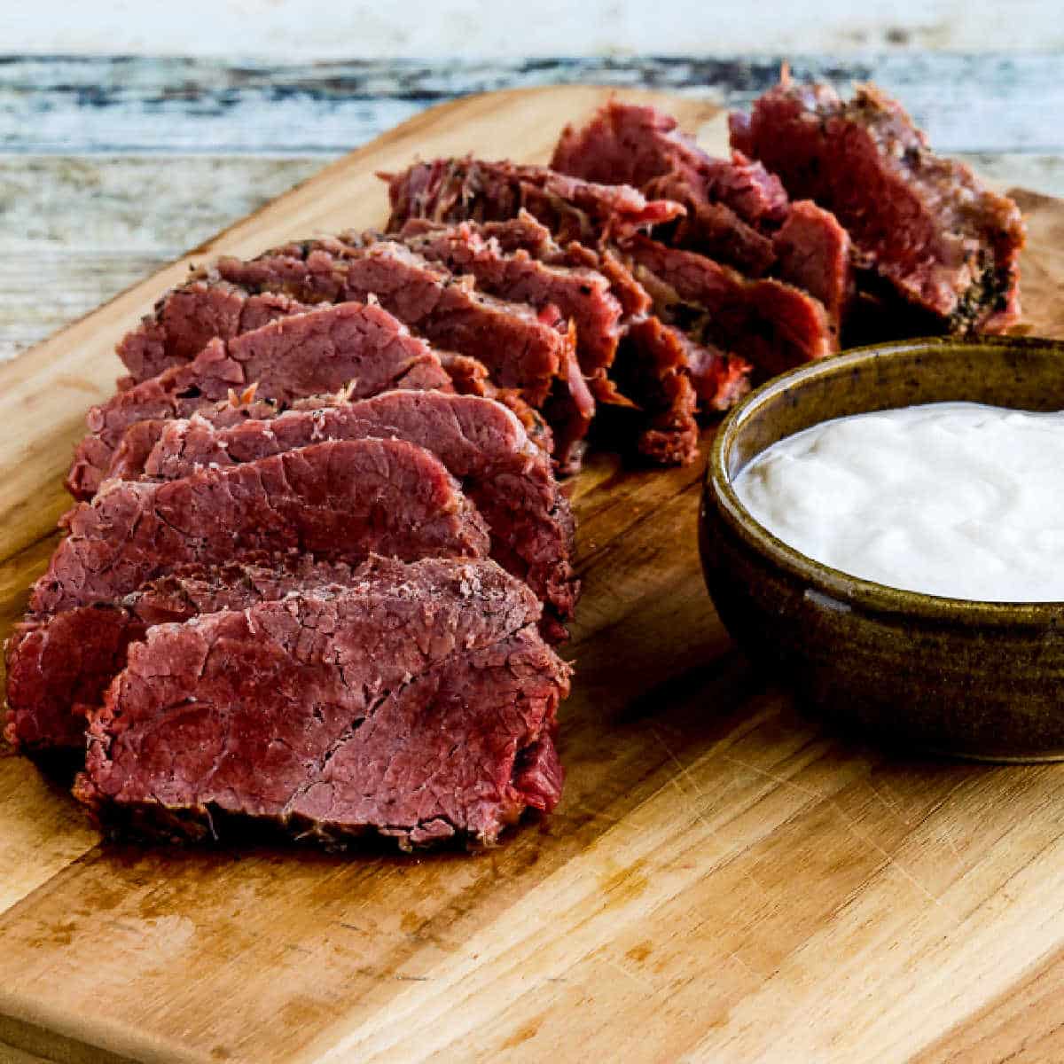Square image of Instant Pot Corned Beef with Creamy Horseradish Sauce shown on a cutting board.