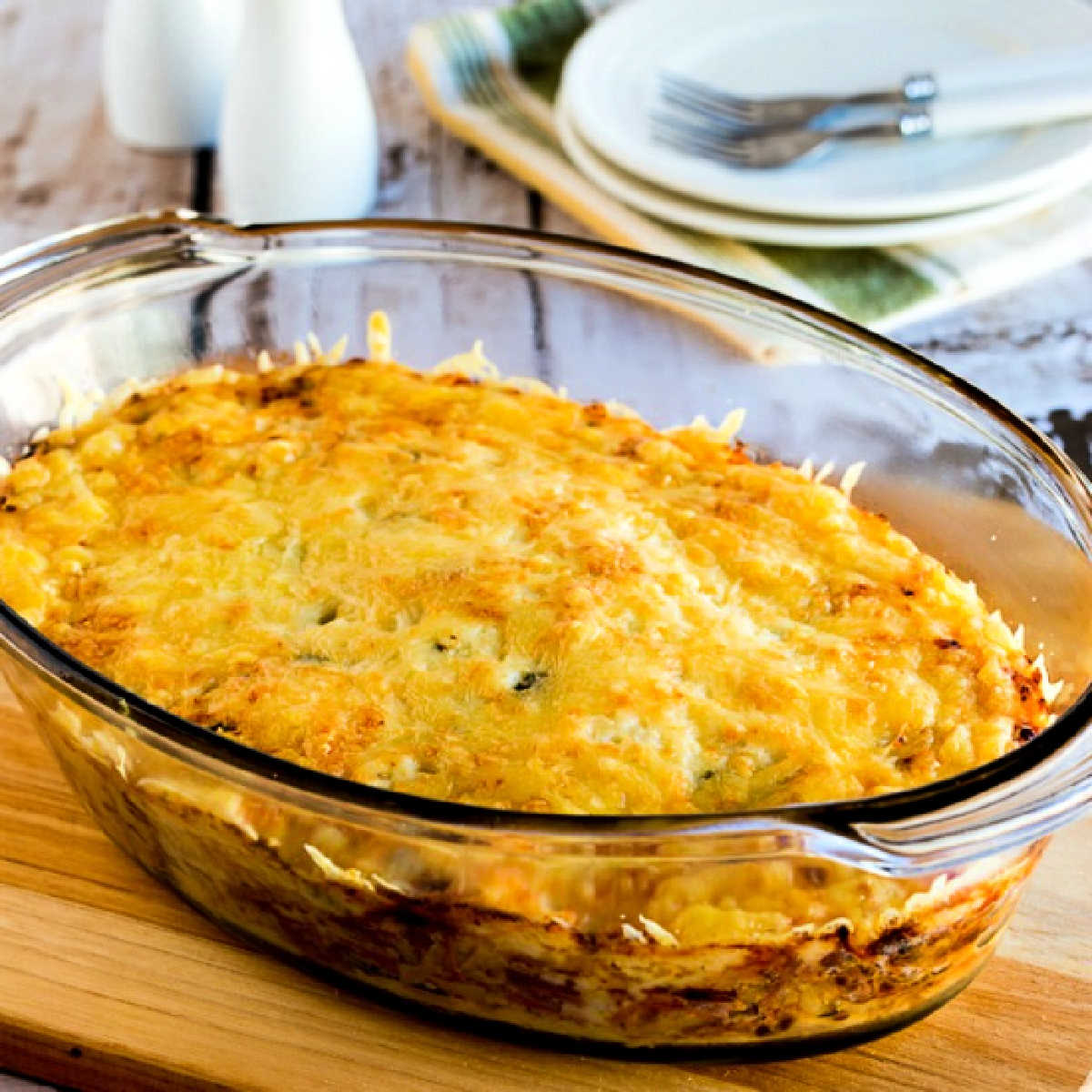 A square image of a low carb Reuben bake presented in a casserole dish with a plate, fork, salt and pepper.