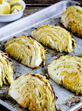 square image of Roasted Cabbage with Lemon shown on baking sheet with cut lemons in background.