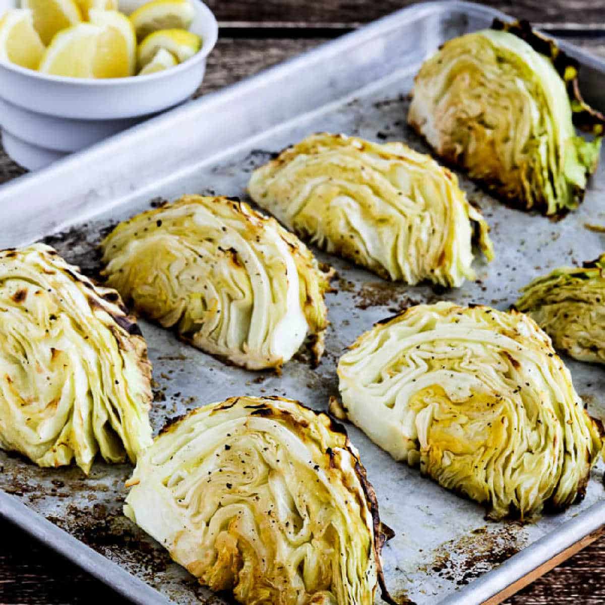 square image of Roasted Cabbage with Lemon shown on baking sheet with cut lemons in background.