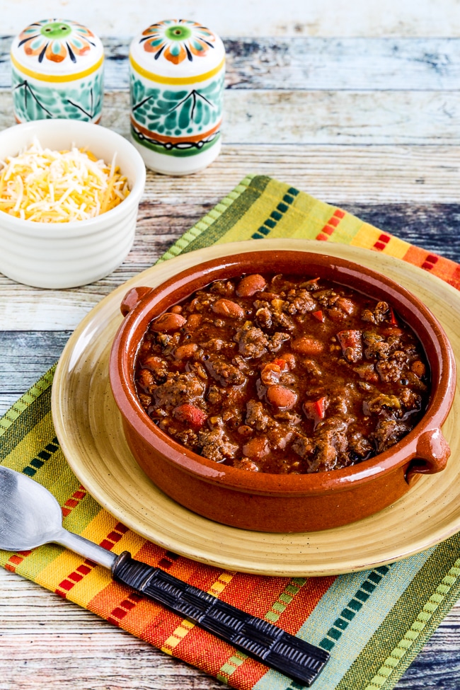 Slow Cooker Beef and Refried Bean Chili shown in serving bowl with condiments in back.