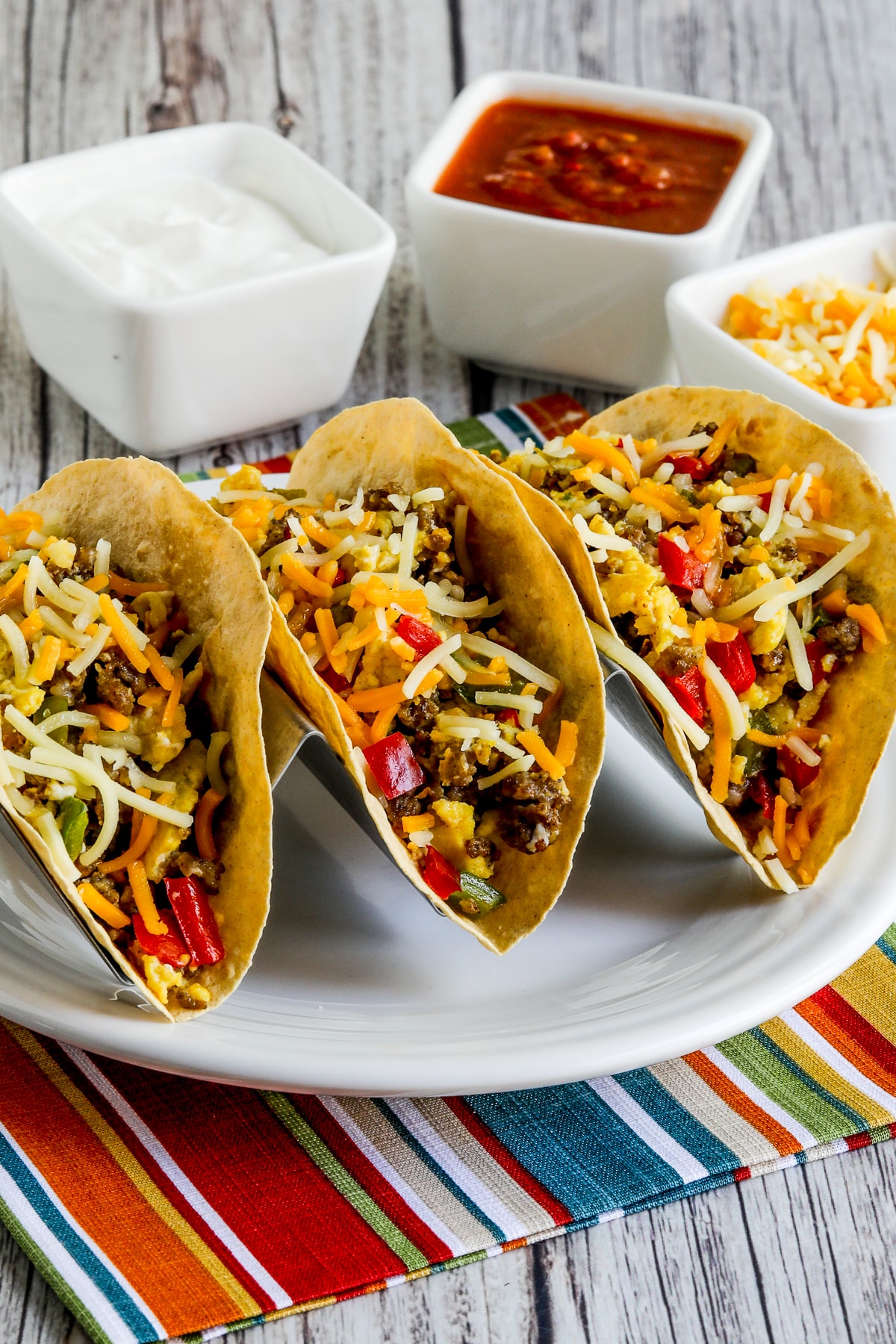 Low-Carb Breakfast Tacos recipe photo showing tacos in holder with sour cream, salsa, and cheese in back.