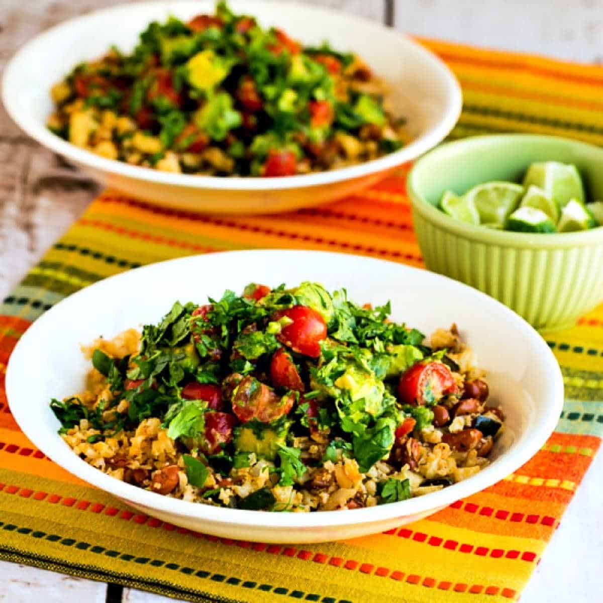 Square image for Cauliflower Rice and Pinto Bean Vegetarian Burrito Bowl shown with two bowls on napkin and bowl of limes on the side.