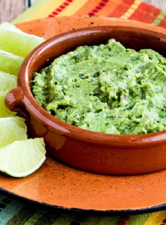 Square image for Cilantro-Lovers Perfect Guacamole showing guacamole in terra cotta dish with limes on the plate.
