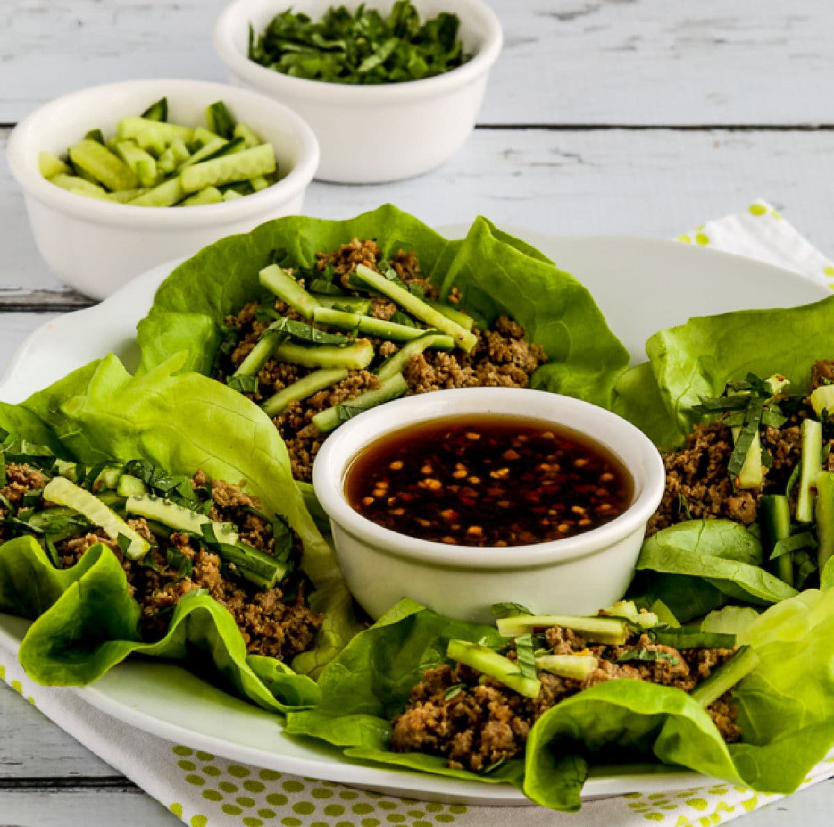 Thai Turkey Lettuce Wraps shown on serving plate with dish of sauce in center.