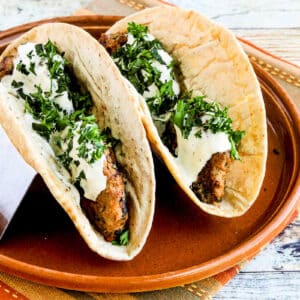 Square image of Grilled Middle Eastern Turkey Burgers shown inside pita bread with sauce, on serving plate.