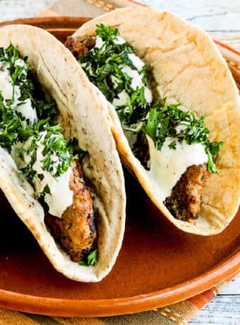 Square image of Grilled Middle Eastern Turkey Burgers shown inside pita bread with sauce, on serving plate.