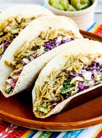 Square image of Green Chile Chicken Tacos shown on serving plate with limes in back.