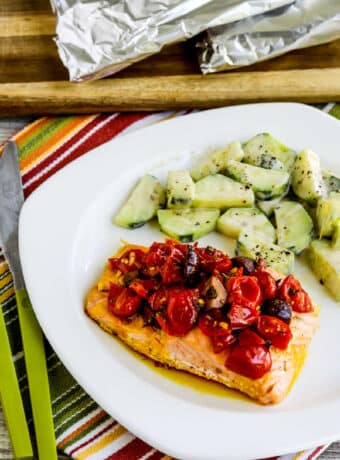 Salmon Foil Packets with Tomatoes and Olives shown on serving plate with cucumber salad