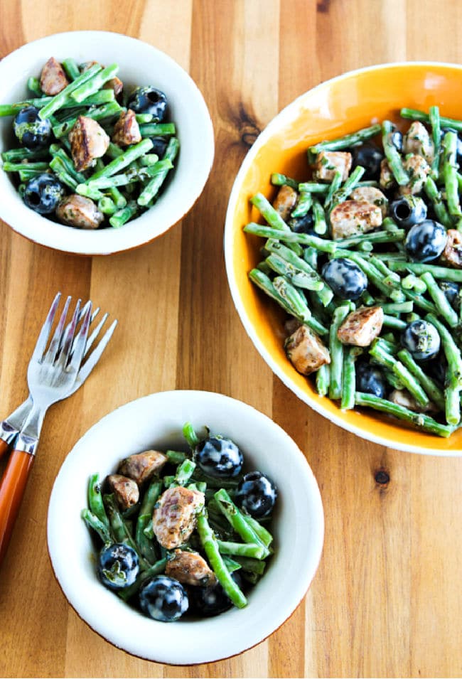 Green Bean Salad with Sausage and Olives on cutting board in large bowl and two small bowls