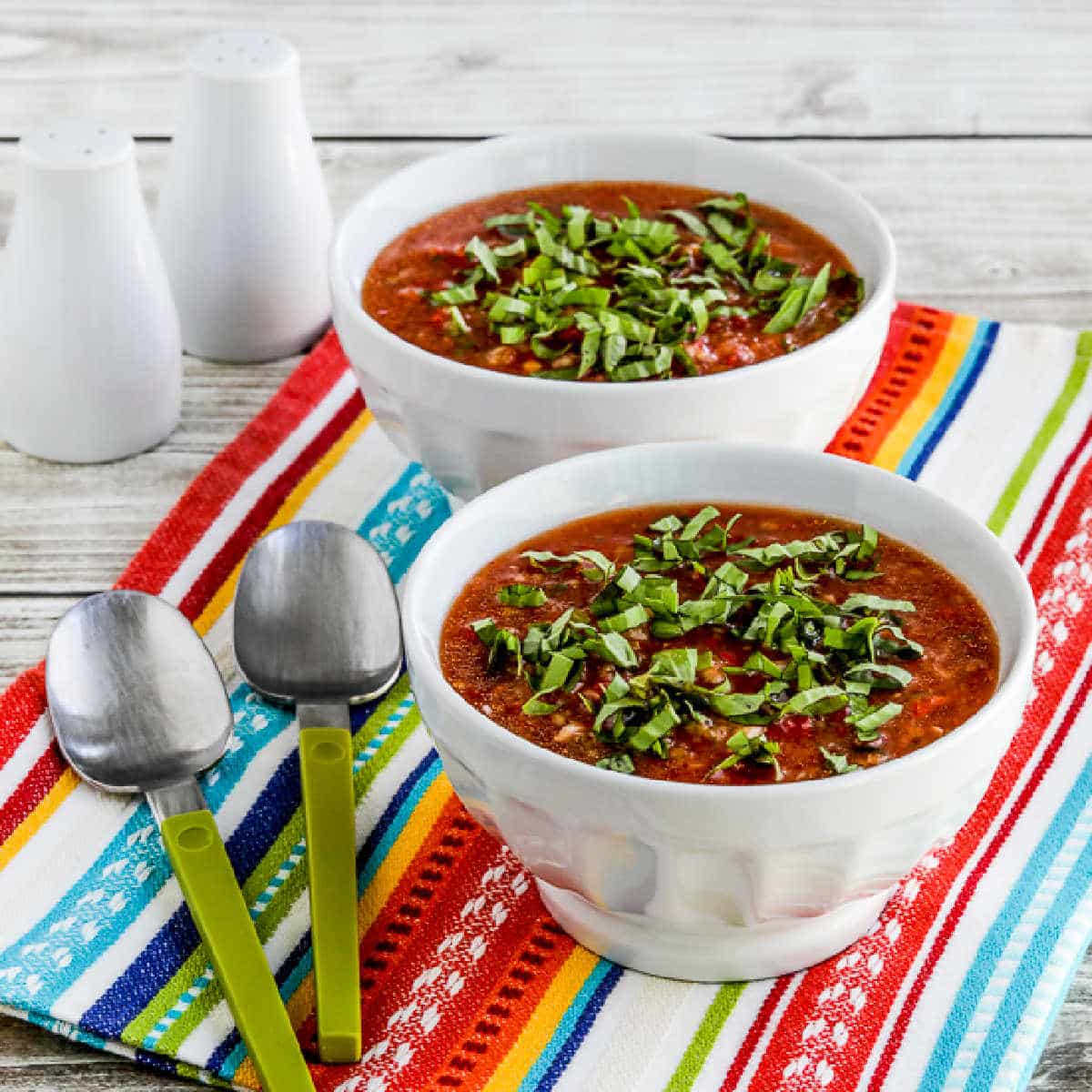 Square image of Gazpacho with Red and Yellow Tomatoes shown in two bowls with green spoons.