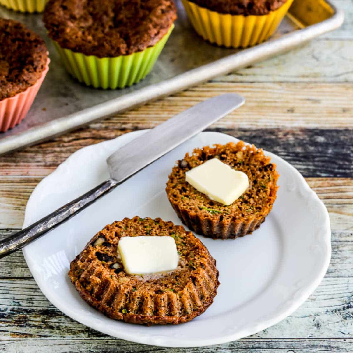 Flourless Keto Zucchini Muffins with one muffin on plate, cut in half, with pats of butter.