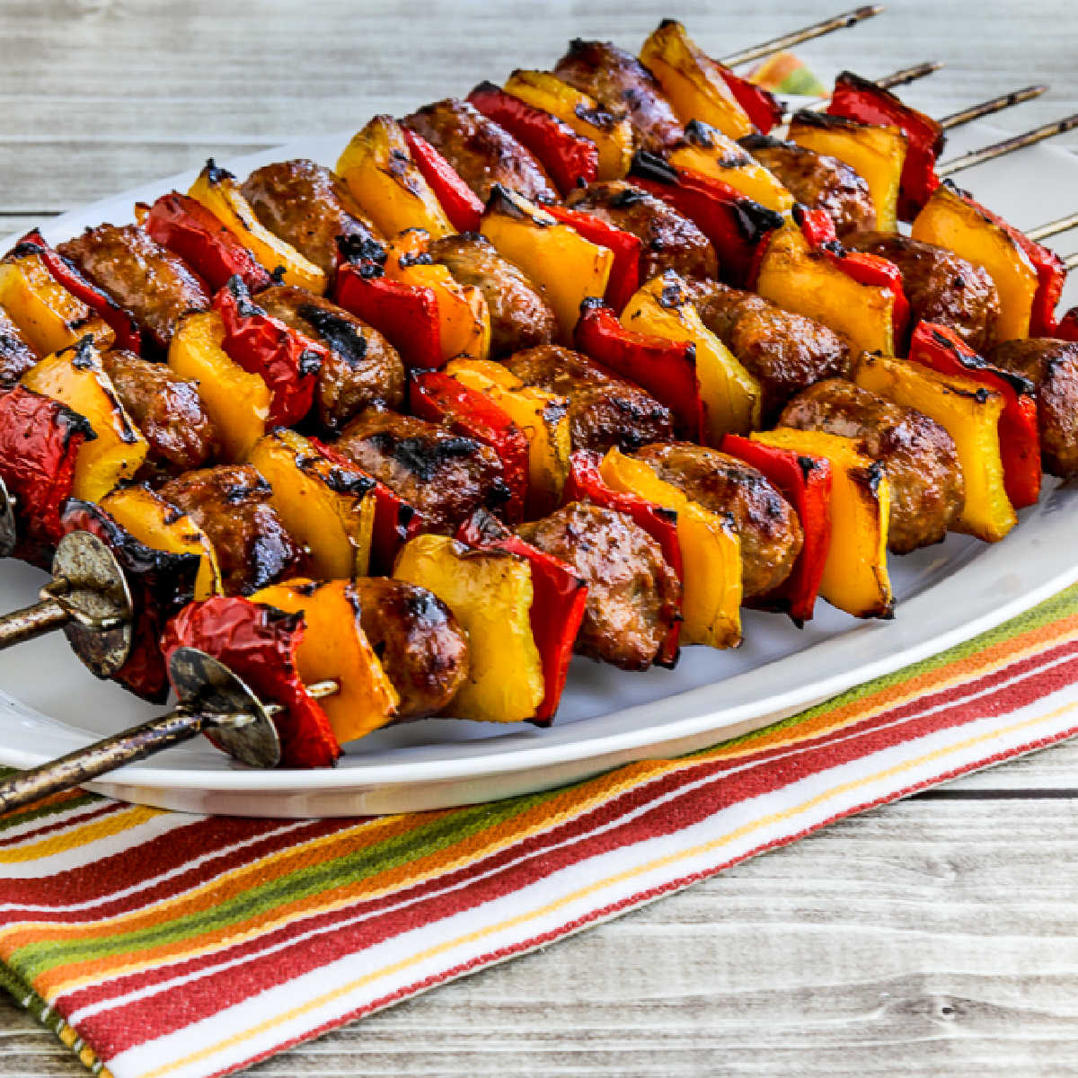 square image of Grilled Sausage and Peppers shown on skewers on serving plate